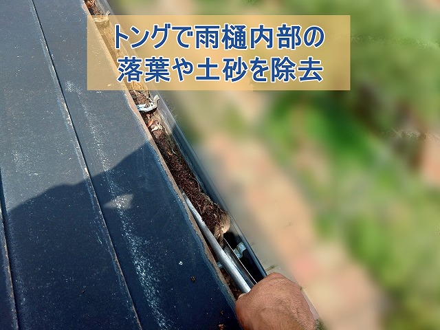 トングで雨樋内部の土砂を取り除いている様子
